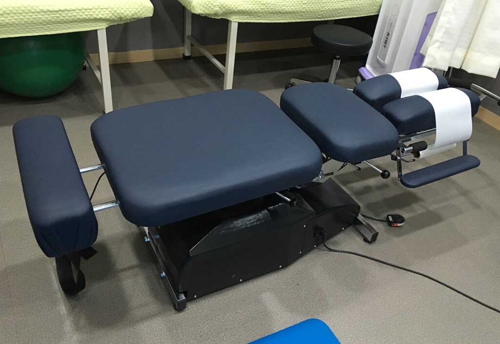 A chiropractor gently adjusts a young athlete's leg while discussing recovery steps in a sunlit treatment room.